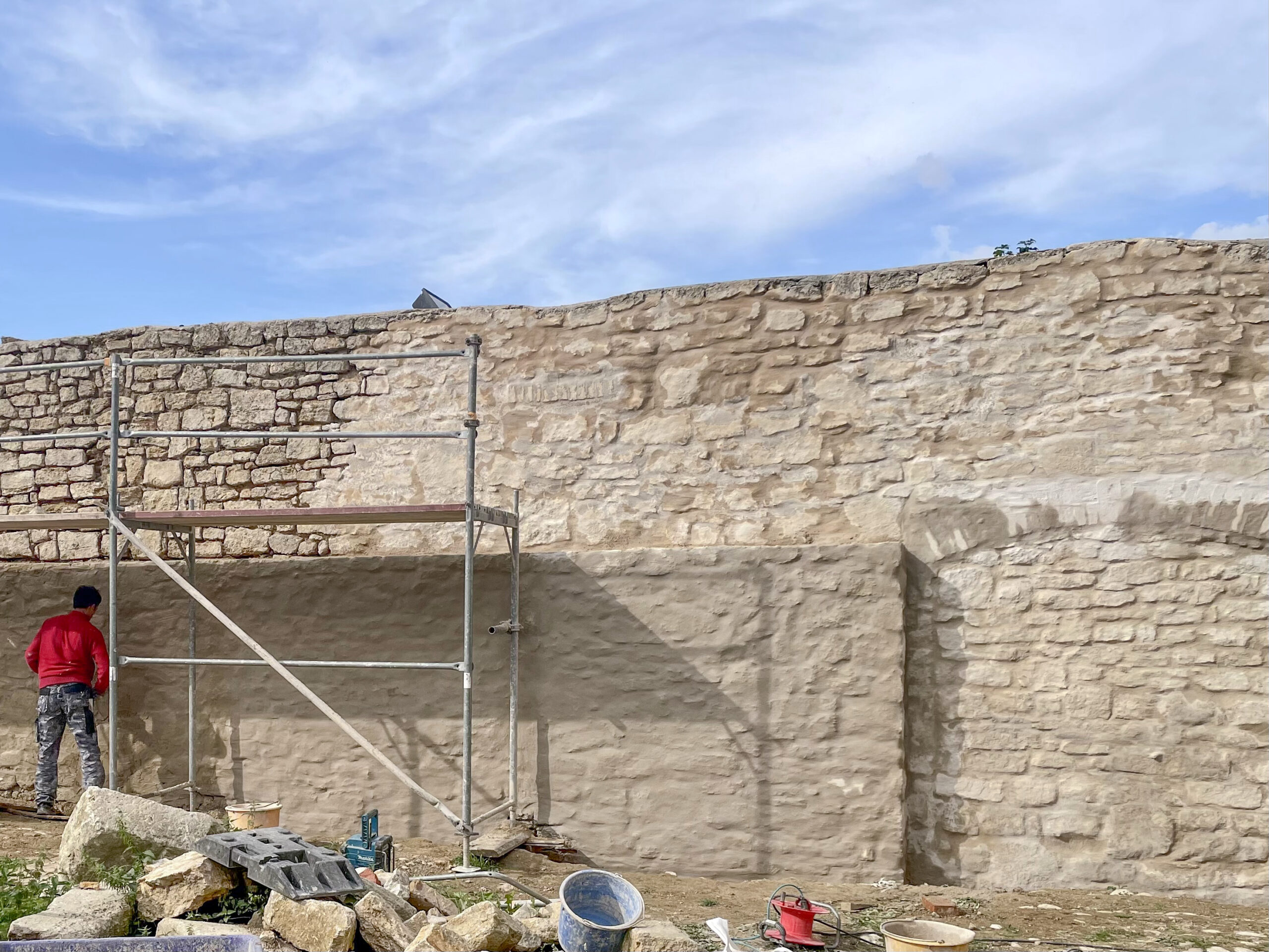 Mann bessert Steinmauer mit Gerüst aus.